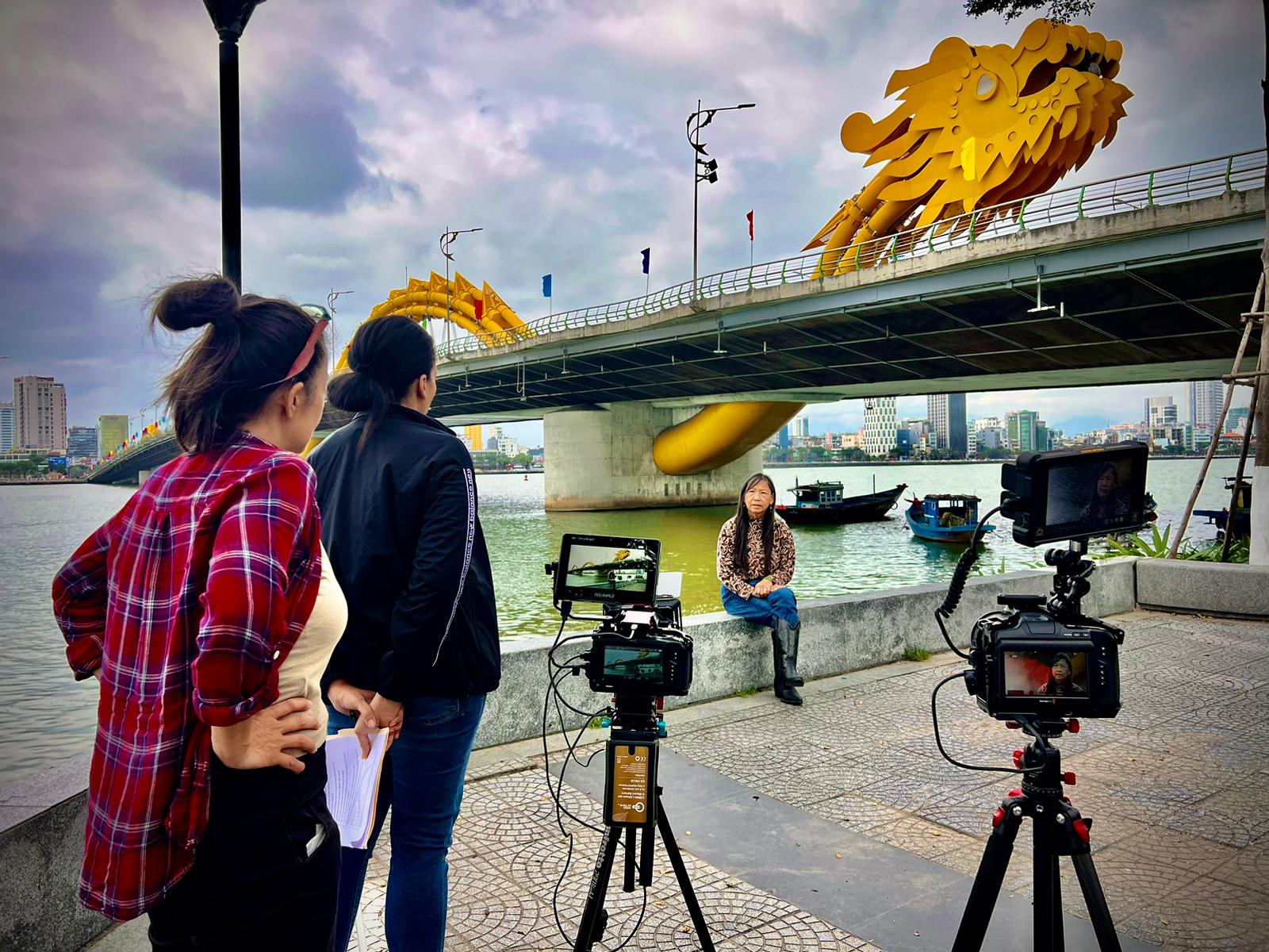 Film crew with cameras on tripods shooting an interview beneath the Dragon Bridge in Da Nang, Vietnam
